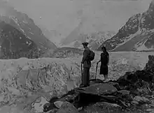 Photo en noir et blanc d'un homme et d'une femme appuyés sur une canne et contemplant le glacier.