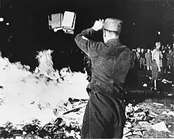 Photo noir et blanc prise de nuit, le 10 mai 1933, d'un autodafé public. Au centre et au premier plan, un homme en uniforme, de dos, lance des livres dans un feu, à sa gauche. À droite, en arrière-plan, un autre milicen surveille quelques badauds.