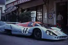 Une Porsche 917 LH garée en pleine rue, devant un hôtel.