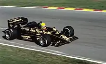 Photographie en couleur d'une Formule 1 noire et or, vue de trois-quarts droit, dans son ensemble.