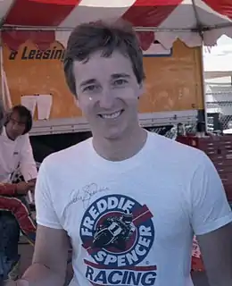 Homme vêtu d'un T-shirt blanc comportant des inscriptions en bleu et rouge.