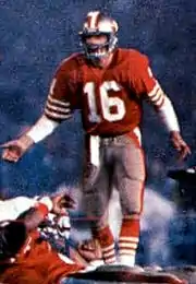 Un joueur de football américain avec un maillot rouge et un numéro 16 blanc les bras ouverts.