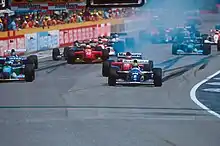 Photo de la ligne droite des stands du Grand Prix de Saint-Marin, peu de temps après le deuxième départ. Senna (voiture bleue et jaune) est en tête devant une vingtaine de voitures.