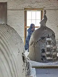 Une femme travaille sur des sculptures en forme de robe bouffante dans un atelier en brique blanche