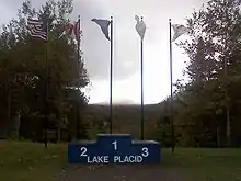 Un podium portant l'inscription « Lake Placid » devant cinq drapeaux.