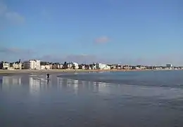 Photographie montrant une grande plage de sable fin de forme courbe à marée basse