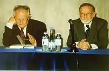 deux hommes assez âgés assis à une table de conférence