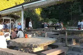 Photographie d'une aire de repas en plein aire sur des tables formées de lauzes.