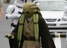 Homme portant un masque vert et un costume marron et crème.