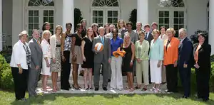 Groupe de joueuses, en tenues civiles, posant avec George W. Bush, au centre, avec un ballon dans les mains.