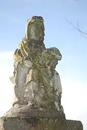 Statue d'une Vierge, couverte de mousse, sur fond de ciel bleu.