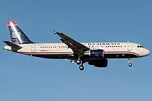 Photo couleur de l'avion, peint d'une longue bande bleu foncé sur la partie supérieure, d'une bande grise sur la partie inférieure et de petites bandes rouge et blanche au milieu du fuselage, roulant sur l'aéroport, avec la banlieue de New York en arrière-plan.