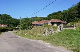 Photographie représentant une petite maison au pied d'une colline boisée.