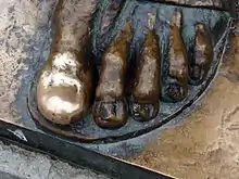 Photographie du pied d'une statue métallique, avec un gros orteil poli et brillant.