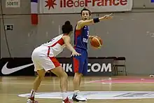 Une joueuse française, balle en main, face à une joueuse canadienne.
