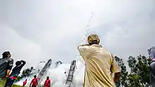 Des hommes debout regardent une fusée partir dans un nuage de fumée depuis une rampe de lancement en bambou ressemblant à une échelle.