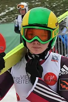 Une femme avec un casque et des skis sur l'épaule.