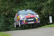 Voiture rouge, bleue et jaune, sautant après une bosse, vue de face.