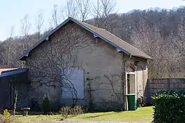 Un petit bâtiment gris avec toit à deux pans et ouverture fermée dans un jardin privé.