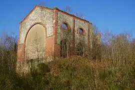 Deux façades aux ouvertures arrondies en demi-arc de cercle ornée de brique rouge, la plus grande ouverture qui occupe entièrement l'une des façade est murée.