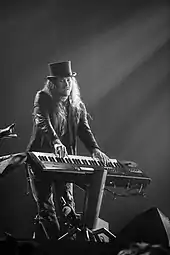 Photo en noir et blanc d'un homme avec un chapeau jouant du clavier sur une scène.