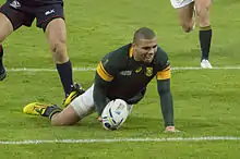 Le joueur sud-africain est au sol avec le ballon dans la main droite.
