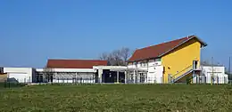 Un bâtiment à étage jaune et un bâtiment de plain-pied blanc encadrant une cours de récréation.