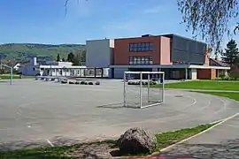 Grand bâtiment cubique blanc et brique derrière une cours de récréation.