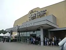 Devanture d'un bâtiment jaune et gris, à l'entrée duquel est écrit en relief « The Making of Harry Potter, Warner Bros Studio Tour ».