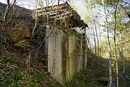 Mur en béton supportant un déversoir rouillé.