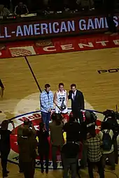 Au milieu d'un terrain de basket-ball, sous les projecteurs, une joueuse reçoit un trophée devant de nombreux photographes.