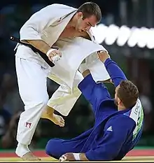 Deux judokas, l'un debout à gauche, l'autre au sol à droite.