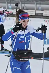 Photographie d'une femme vêtu d'un survêtement blanc et bleu et tenant des bâtons de ski