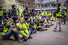 Rassemblement de Gilets jaunes à Bruxelles, principalement des hommes. Quelques-uns sont assis au premier plan.