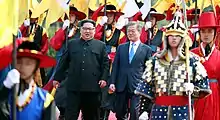 Des militaires en costumes traditionnels accompagnent Kim Jong-un et Moon Jae-in qui marchent côte à côte.