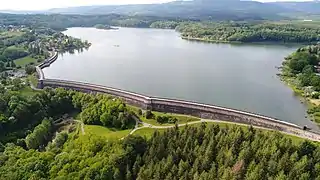 Un vaste plan d'eau retenu par une muraille entouré de forêts.