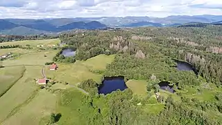 Plusieurs étangs sur une colline couverte de prairies et de forêts devant un panorama montagnard.