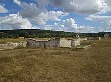 Présentation d'édifices en ruines adossé à un mur.