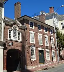 Photographie en couleur des bâtiments le long de Thomas Street à Providence, Rhode Island. La maison Seril Dodge en brique, à droite, comporte trois étages. Elle possède une grande porte en bois, au-dessus de laquelle est suspendue une lampe. Une petite enseigne en fer indiquant Providence Art Club est suspendue sur le côté du bâtiment, au-dessus du trottoir. Une petite arche en brique la relie à l'autre Seril Dodge House à gauche, juste hors de vue.