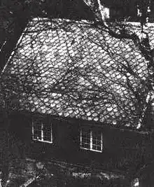 Prise de vue en hauteur d'une maison aux tuiles apparentes ; le ton de la photographie est sombre.
