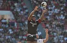 Joueur en l'air, tendant les deux bras en avant pour prendre un ballon en touche.