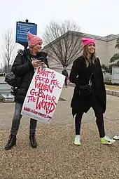 Deux femmes avec des bonnets roses portent un panneau disant "What's good for women is good for the world"