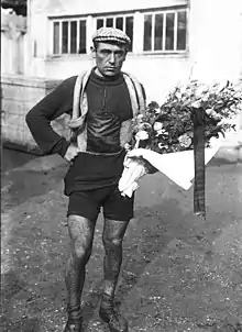 Photographie en noir et blanc d'un homme en tenue de cycliste portant un bouquet de fleurs dans la main gauche.