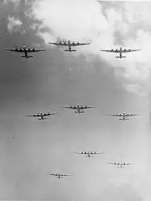 Photographie noir et blanc de bombardiers en formation dans le ciel (vue depuis le sol).
