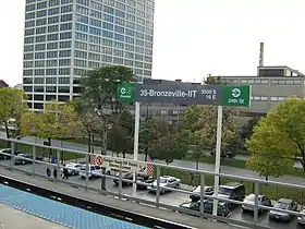 Un panneau de la station et vue de la rue. Le panneau indique que la sortie avec ascenseur est à gauche