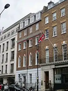 Photographie en couleur d'une rue de Londres, une voiture au premier plan et plusieurs bâtiments en arrière plan, dont l'un arbore le drapeau du Royaume-Uni.