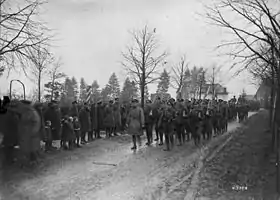 Photographie en noir et blanc de militaires marchant sur un chemin avec d'autres militaires se tenant sur le côté du chemin