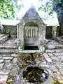 La fontaine Saint-Quirin avec son bassin rond servant aux ablutions des malades et deux statues de la Vierge et de Saint-Quirin dans sa niche.