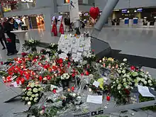 Photo rapprochée d'un ensemble de fleurs et bougies disposées sur le sol près d'un pilier dans un hall d'aéroport.