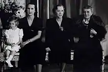 quatre générations féminines posent côté à côte. De gauche à droite on voit une fillette assise et vêtue de clair, puis trois femmes vêtues de sombre